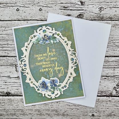 Handmade sympathy card with ornate oval frame, gold sympathy quote “those we love don’t go away, they walk beside us every day,” teal watercolor background with blue flowers and sparkling gem accents. Envelope included.