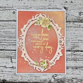 Handmade sympathy card with ornate oval frame, gold sentiment reading “those we love don’t go away, they walk beside us every day,” coral watercolor background, floral accents, and rhinestone embellishments.